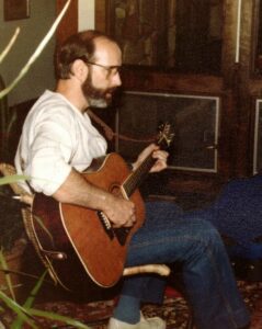 A man sitting down playing an acoustic guitar.