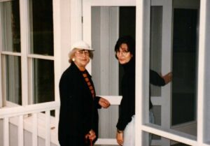 Two women standing in a porch with one woman wearing a white hat.