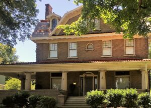 A large brick house with a porch and trees.