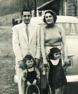 A man and woman standing with two children in front of an old car.