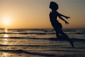 A person jumping in the air on top of a beach.